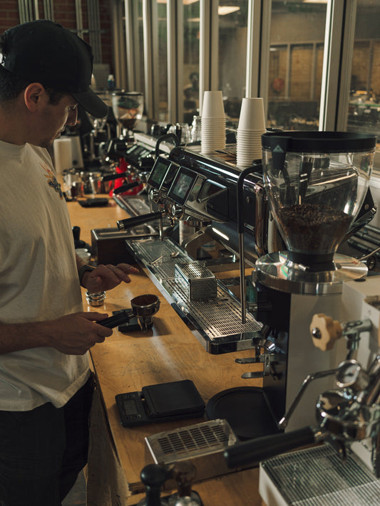 A barista working on commercial espresso machine. He is making a latte from an espresso shot. 